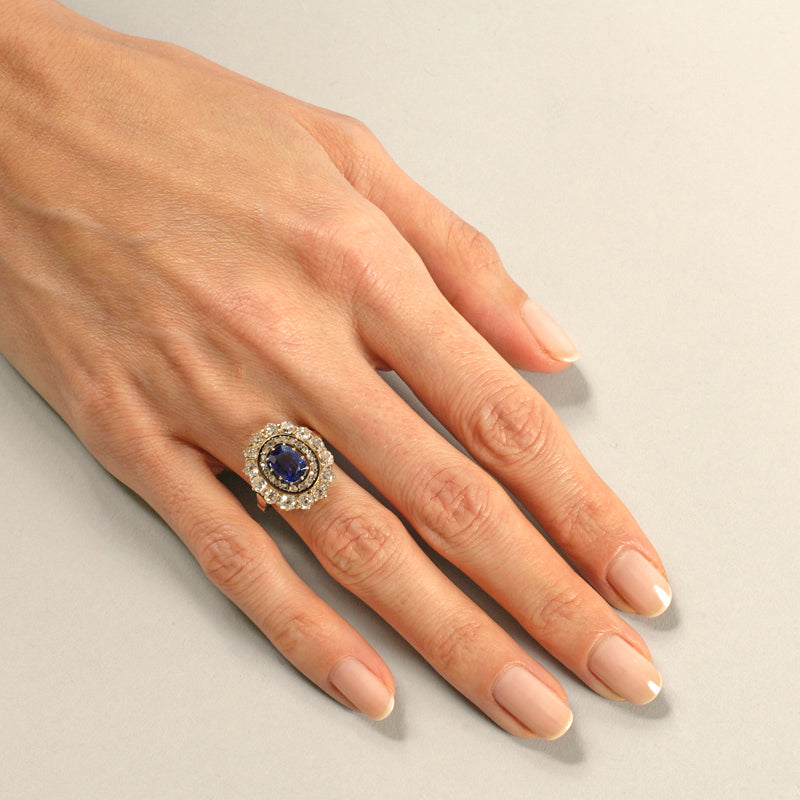 Macklowe Gallery An English Antique 15 karat gold/silver top ring with sapphire and diamonds. The ring centers on a no heat oval-cut sapphire with an approximate weight of .95 carat, 14 old mine-cut diamonds with an approximate total weight of 1.40 carats, and 19 rose-cut diamonds with an approximate total weight of .19 carat.  Designed in a classic oval cluster motif.